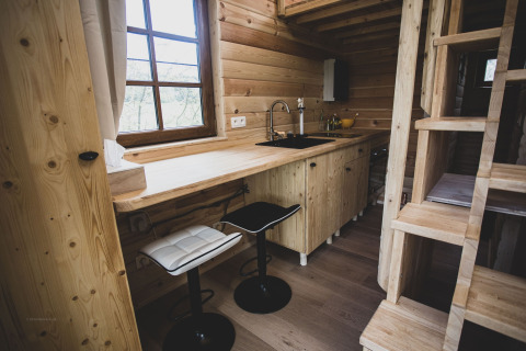 Modern treehouse kitchen with bar stools, wood paneling, window, and staircase in Belgium’s Bird Nest.
