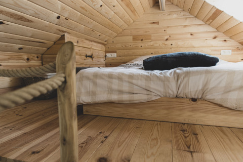 Cozy sleeping area with low bed and wood paneling in the «Bird Nest» tree house, Belgium, interior view.