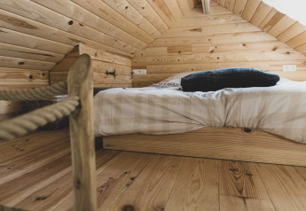 Zona notte accogliente con letto basso e rivestimenti in legno nella «Bird Nest», casa sull'albero in Belgio.
