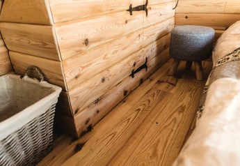 Gemütlicher Innenraum eines Baumhauses in Belgien mit Holzboden, Truhe, Wäschekorb und Hocker.