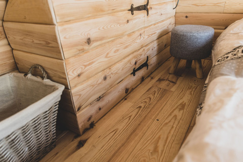 Interno accogliente della casa sull’albero Bird Nest in Belgio con pavimento, cesta e sgabello in legno.