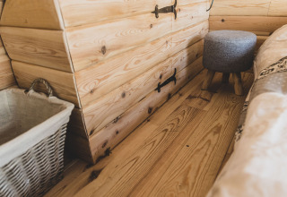 Interno accogliente della casa sull’albero Bird Nest in Belgio con pavimento, cesta e sgabello in legno.