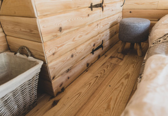 Interno accogliente della casa sull’albero Bird Nest in Belgio con pavimento, cesta e sgabello in legno.