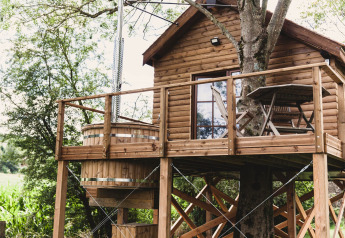Baumhaus namens „Bird Nest“ in Belgien mit Holzterrasse, Sitzgruppe und Outdoor-Badewanne.