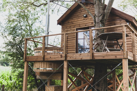 Treehouse called “Bird Nest” in Belgium with a wooden deck, outdoor table set, and a hot tub outside.