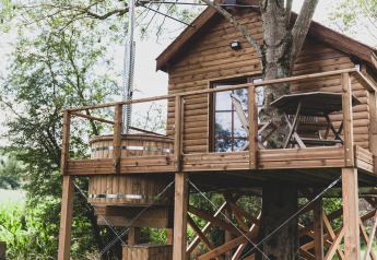Casa sull’albero chiamata “Bird Nest” in Belgio con terrazza in legno, tavolo e vasca idromassaggio.