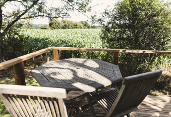 Holztisch und Stühle auf Terrasse mit Blick auf Felder, vom Baumhaus Bird Nest in Belgien aus gesehen.