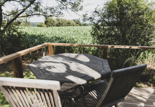Wooden patio table and chairs on deck with a scenic view of fields, at Bird Nest treehouse in Belgium.