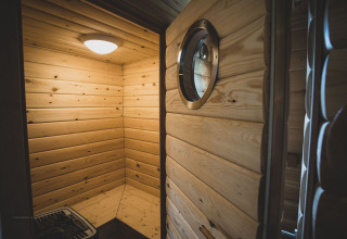 Interior view of a cozy, modern treehouse sauna with wood paneling and round window in Belgium.