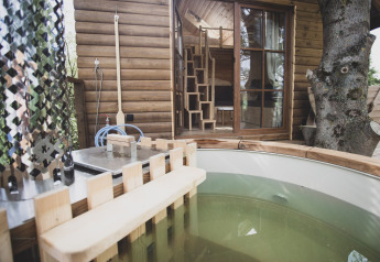 Vasca da bagno esterna davanti a una casa sull'albero con pareti in legno in Belgio, immersa nella natura.