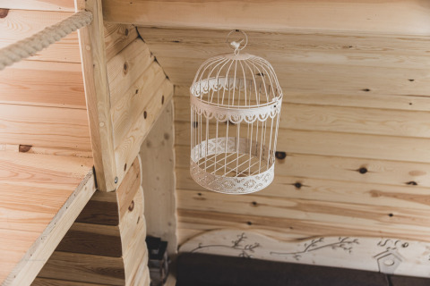 Interno di una casa sull'albero in Belgio: una gabbia decorativa vuota appesa a un soffitto di legno chiaro.