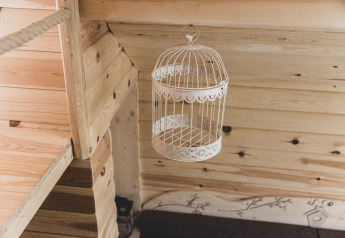 Interno di una casa sull'albero in Belgio: una gabbia decorativa vuota appesa a un soffitto di legno chiaro.