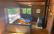 Gezellige houten woonkamer in chalet 'La Bressine' in België met zetels, groot raam en kachel.