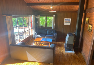 Houten woonkamer in chalet 'La Bressine' in België met banken, groot raam en verwarming.
