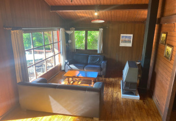 Gezellige houten woonkamer in chalet 'La Bressine' in België met zetels, groot raam en kachel.