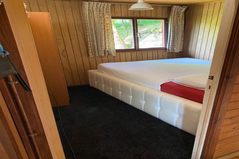Slaapkamer in een houten chalet met groot wit bed, ramen en gebloemde gordijnen in België.