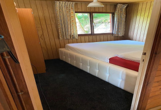 Slaapkamer in een houten chalet met groot wit bed, ramen en gebloemde gordijnen in België.