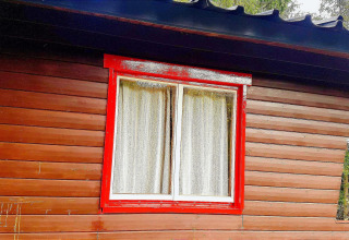 Een raam met een rode omlijsting en witte gordijnen aan chalet La Bressine in België.