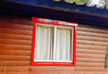 Raam met rood geschilderd kozijn en witte gordijnen aan chalet La Bressine in België.