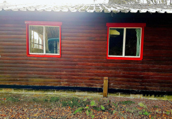 Een chalet La Bressine in België met bruine houten gevel, rode raamkozijnen en reflecterende ramen.