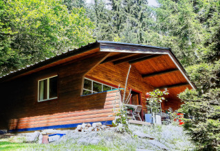 'La Bressine' houten chalet in België, omgeven door bomen en natuur, gefotografeerd op een zonnige dag.