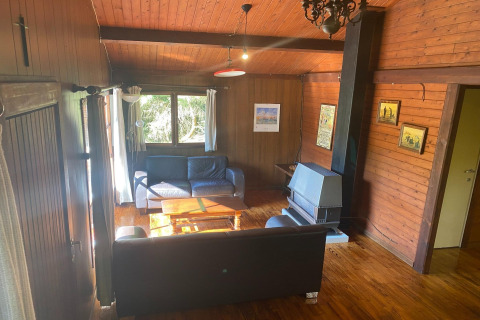 Woonkamer in chalet La Bressine in België met houten wanden, banken, kachel en grote ramen.