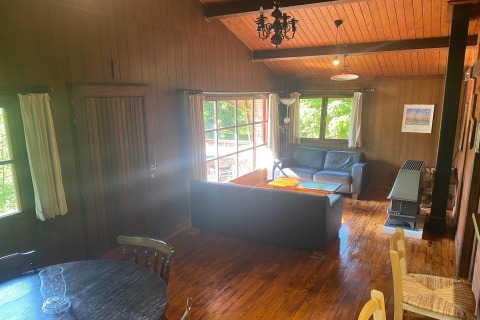 Knusse woonkamer in chalet La Bressine in België met houtafwerking, grote ramen en comfortabele banken.