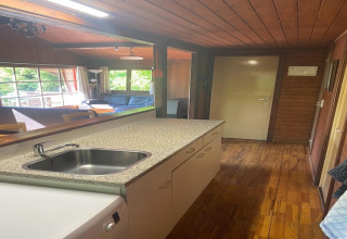 Keuken en woonkamer van chalet La Bressine in België, met houten wanden en grote ramen voor licht.