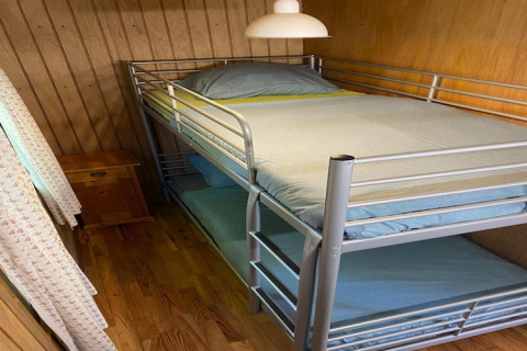 Kleine kamer in chalet La Bressine in België met metalen stapelbed en houten wandbekleding.