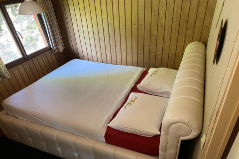 Slaapkamer in chalet La Bressine in België met een tweepersoonsbed tegen houten wandpanelen.