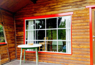 Houten terras met groene tafel en roodomrand raam bij chalet 'La Bressine' in België.