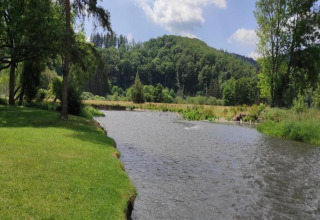 Rivierzicht bij chalet La Bressine in België, met groene grasvelden, bomen en beboste heuvels.