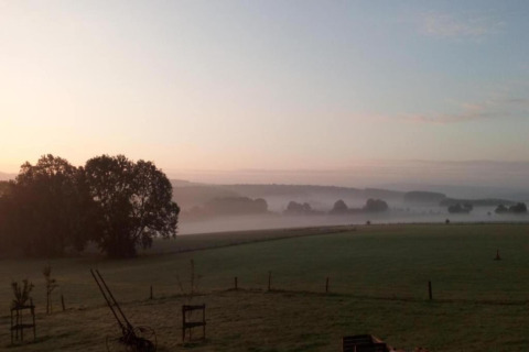 Landelijk uitzicht bij zonsopkomst met mist, velden en bomen, gezien vanaf chalet La Bressine in België.