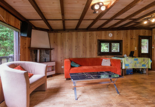 Woonkamer in lodge Le Chession in België, met houten wanden, oranje bank en uitzicht op het bos buiten.