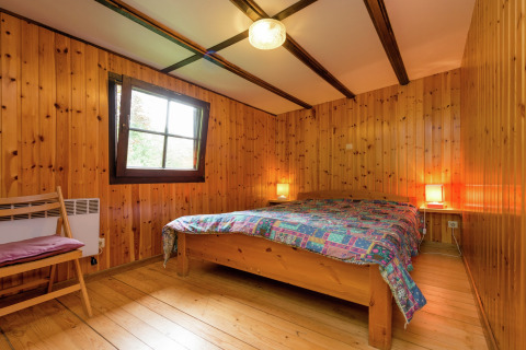 Slaapkamer met houten wanden, tweepersoonsbed en kleurrijk deken bij lodge Le Chession in België.