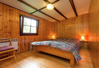 Slaapkamer met houten wanden, tweepersoonsbed en kleurrijk deken bij lodge Le Chession in België.