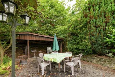 Buiten zitgedeelte bij lodge 'Le Chession' in België met plastic stoelen, tafel en veel groen.
