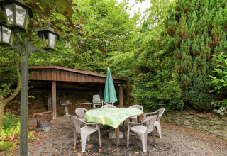 Buiten zitgedeelte bij lodge 'Le Chession' in België met plastic stoelen, tafel en veel groen.
