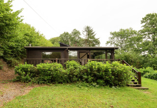Houten lodge bij Le Chession in België, omgeven door groene natuur, frontaal gezien met veranda.