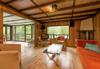 Wohnzimmer in der Lodge 'Le Chession' in Belgien mit Holzwänden, großen Fenstern und Waldblick.