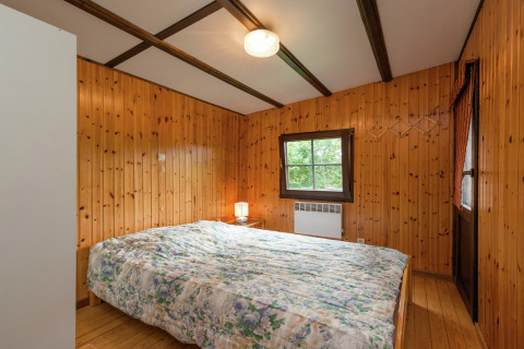 Slaapkamer met houten wanden, tweepersoonsbed en lamp in de Le Chession lodge in België.