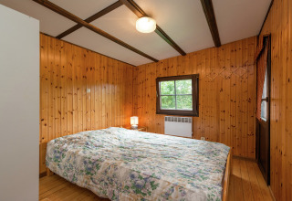 Slaapkamer met houten wanden, tweepersoonsbed en lamp in de Le Chession lodge in België.