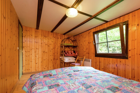 Slaapkamer met houten wanden, tweepersoonsbed en raam in de lodge Le Chession in België.