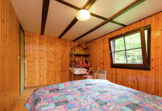 Slaapkamer met houten wanden, tweepersoonsbed en raam in de lodge Le Chession in België.