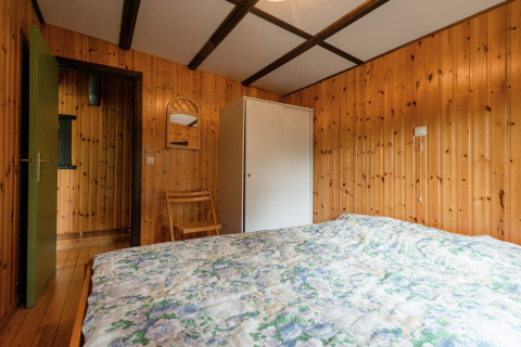 Slaapkamer met houten wanden, bed en kast in de lodge Le Chession in België, sfeervol ingericht.