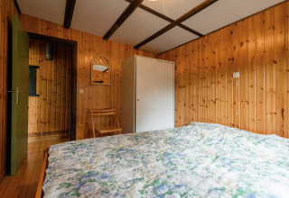 Slaapkamer met houten wanden, bed en kast in de lodge Le Chession in België, sfeervol ingericht.