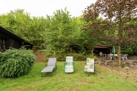 Buitenruimte van lodge Le Chession in België met ligstoelen, terrasstoelen en weelderig groen.