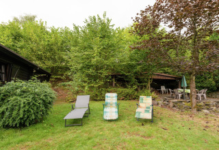 Buitenruimte van lodge Le Chession in België met ligstoelen, terrasstoelen en weelderig groen.