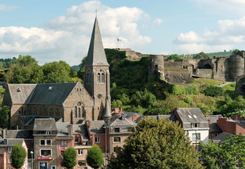 Blick auf die Lodge Le Chession in Belgien mit einer Kirche und einer alten Burgruine im grünen Tal.