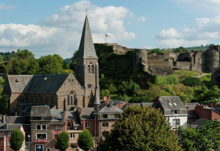 Uitzicht vanaf lodge Le Chession in België, met een oude kerk en kasteel tussen groen in het landschap.